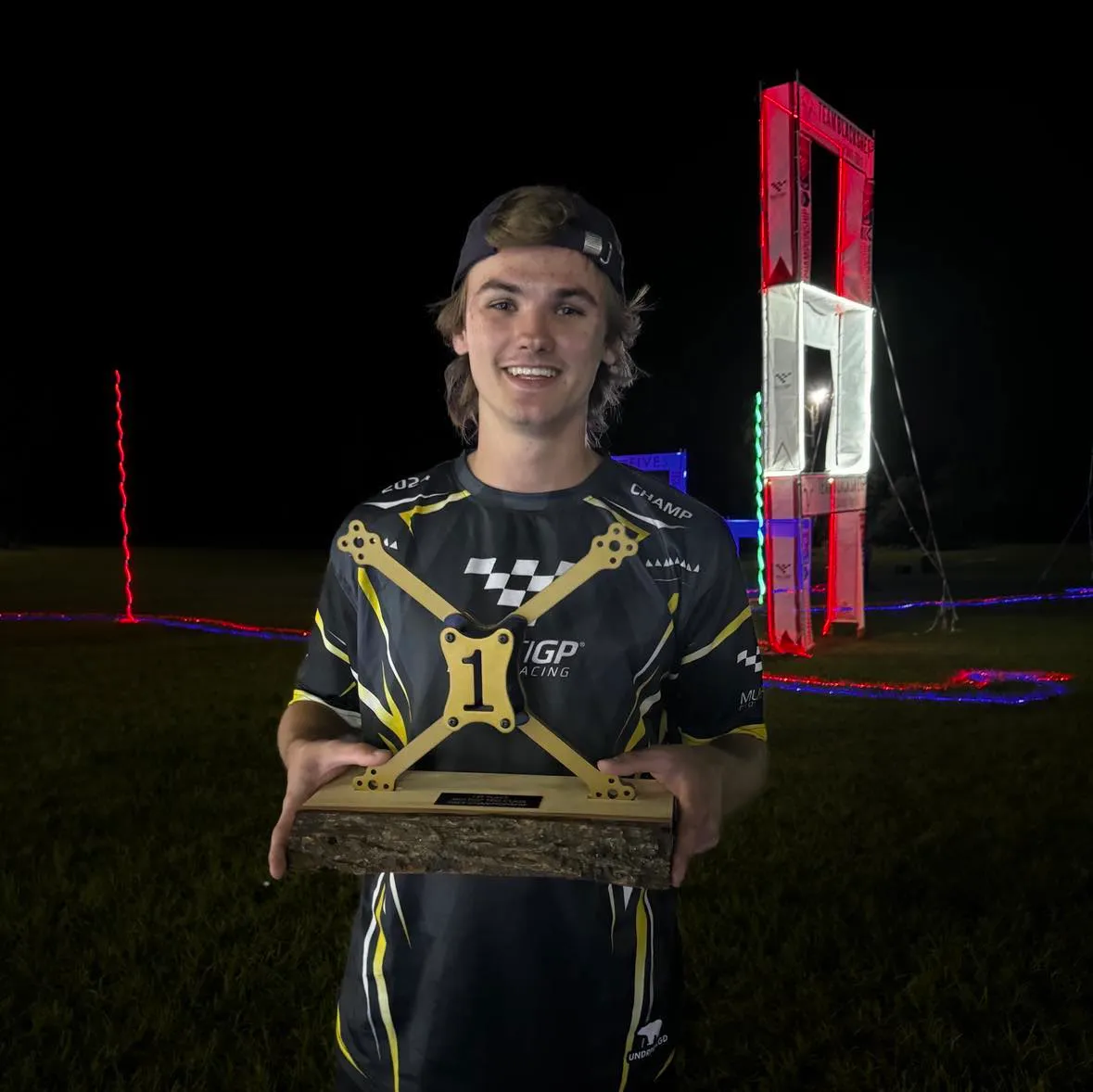 Paweł Laszczak holding the MultiGP Championship trophy at night